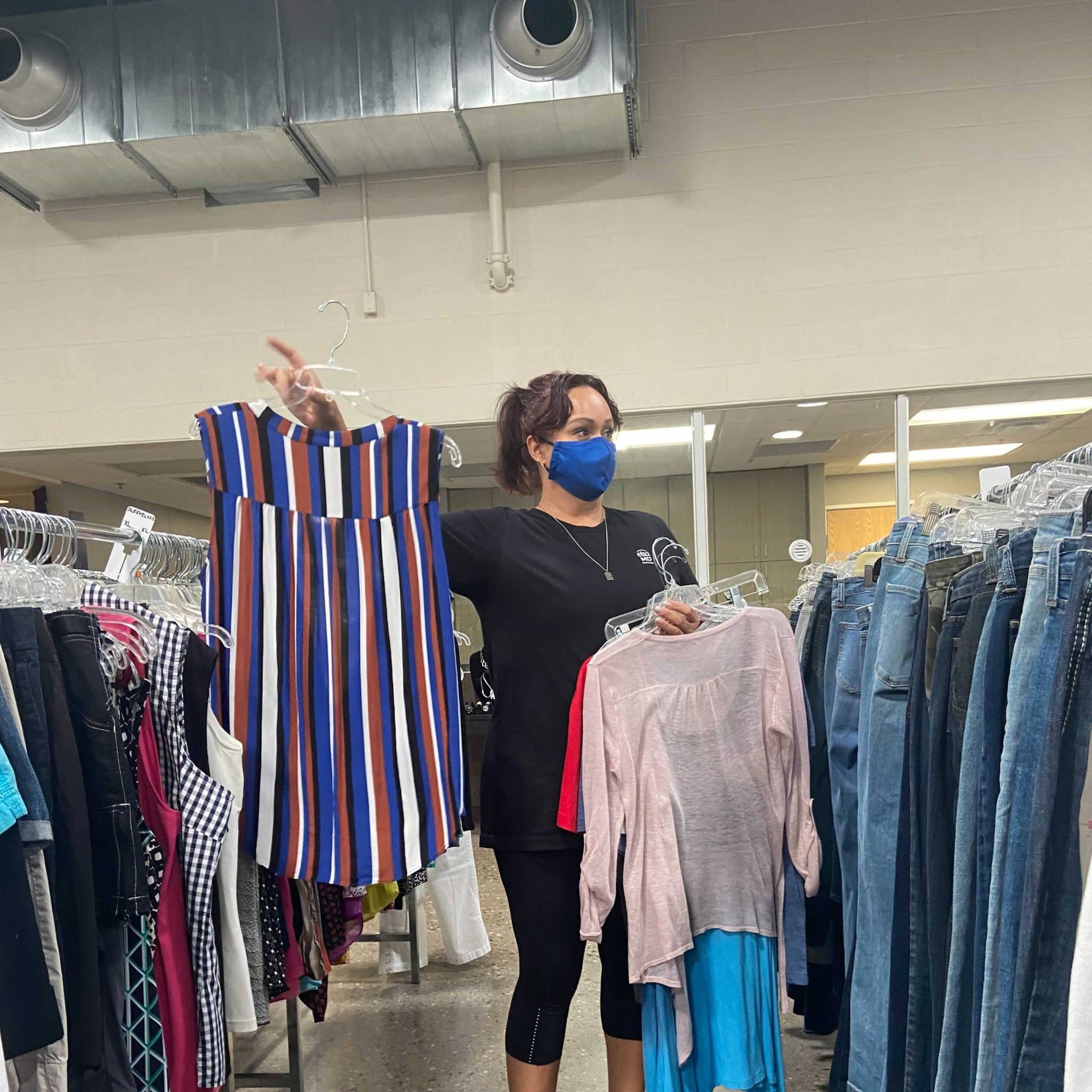 a woman wearing a face mask standing in a store with clothes on swingers